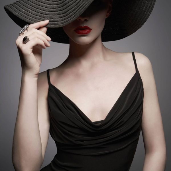 portrait of young lady with black hat and evening dress Fashion portrait of young sexy lady with beautiful black hat and evening dress. Stylish elegant woman with modern jewelry. Studio photo of pretty model on grey background.