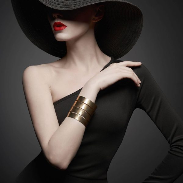 portrait of young lady with black hat and evening dress Fashion portrait of young sexy lady with beautiful black hat and evening dress. Stylish elegant woman with modern jewelry. Studio photo of pretty model on grey background.