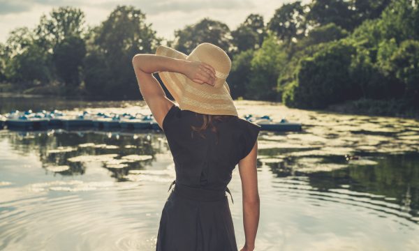 Elegant woman with hat by lake Vintage filtered shot of an elegant woman wearing a hat standing by a lake in a park at sunset
