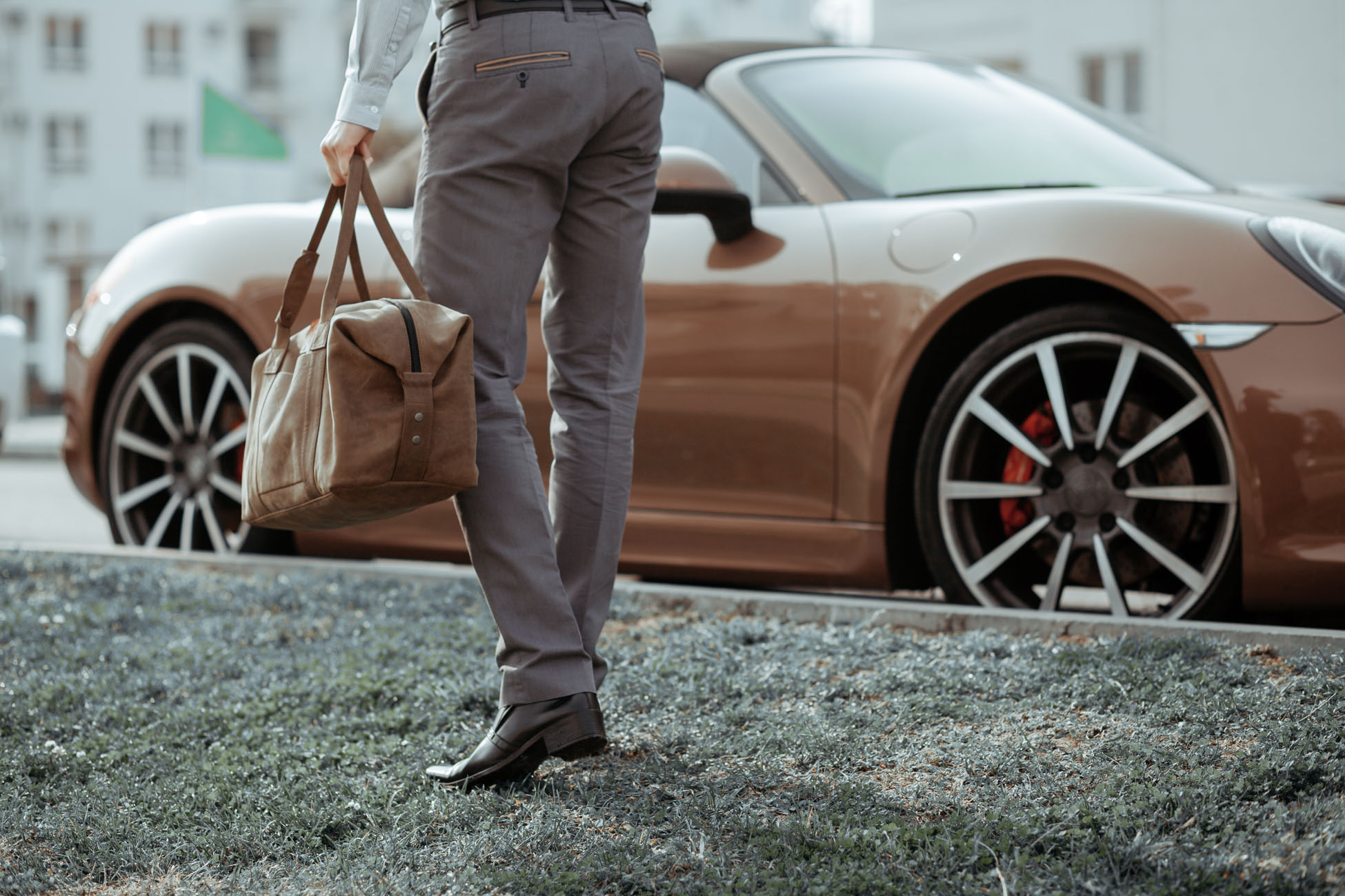 Cool man beautiful model outdoors, city style fashion. A handsome man model walking in the city center next to some cars. urban setting. The young boy as trendy, modern clothing with bag.